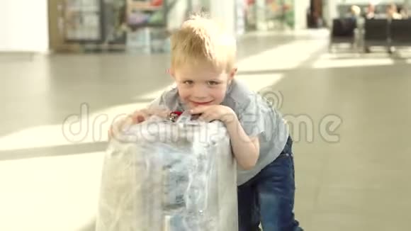 可爱的快乐小男孩在航班前在国际机场带着一个大手提箱视频的预览图