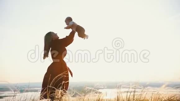 年轻女子把婴儿抛起来抓起来在夕阳的背景下视频的预览图