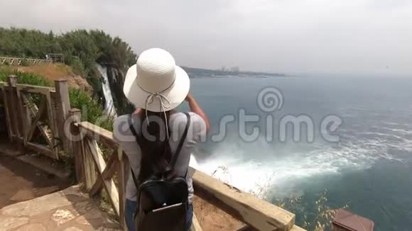 戴帽子的女孩拍了一个非常漂亮的瀑布在海边的视频视频的预览图