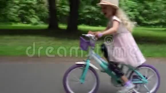 兴奋的金发小女孩穿着粉红色的裙子骑着一辆儿童自行车上路视频的预览图