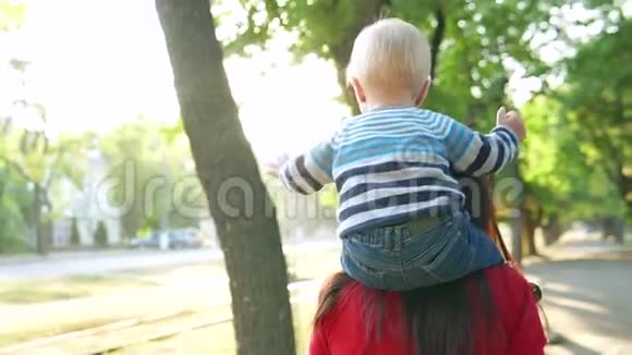 年轻的母亲和她的小儿子微笑着在公园里散步一个男孩坐在一个穿红色毛衣的女孩身上视频的预览图