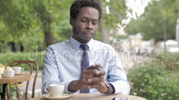 等待的非洲商人在室外咖啡厅喝咖啡和检查时间视频的预览图