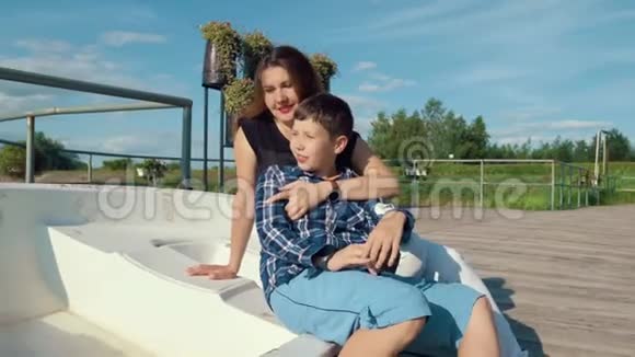 母亲和儿子坐在木墩上的船上享受着乡村的乐趣视频的预览图