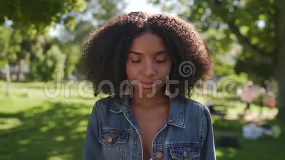 一位年轻的非裔美国妇女站在公园里微笑着看镜头的肖像视频的预览图