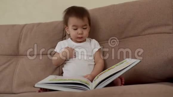 小女孩坐在柔软的沙发上微笑着翻开一本五颜六色的书页视频的预览图