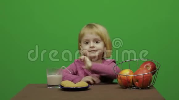 女孩坐在桌子旁吃苹果快乐的三岁女孩可爱的女孩微笑34岁金发女孩视频的预览图