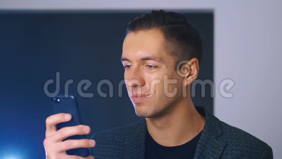 年轻英俊的商人用他的智能手机在办公室背景看着相机和微笑商务视频的预览图