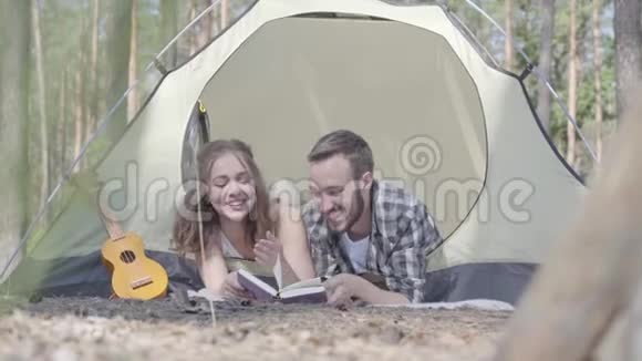 肖像年轻男子漂亮的年轻女子躺在森林里的帐篷里在看书柴禾在里面视频的预览图