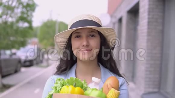 一个年轻漂亮的女人穿着牛仔夹克和帽子带着一个购物袋心情愉快微笑着关闭视频的预览图