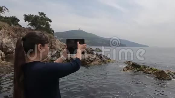 一个亚洲女孩站在土耳其的岩石海滩上为美丽的风景拍照视频的预览图