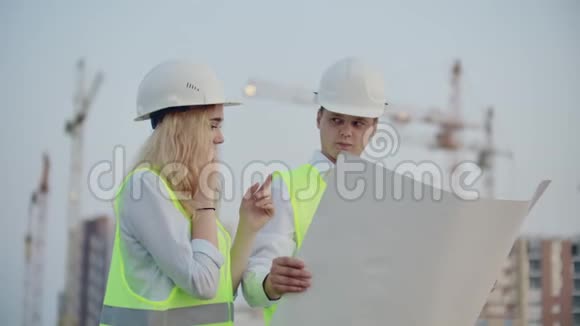 两名建筑工人在正在施工的建筑背景上画着头盔和背心一名妇女视频的预览图