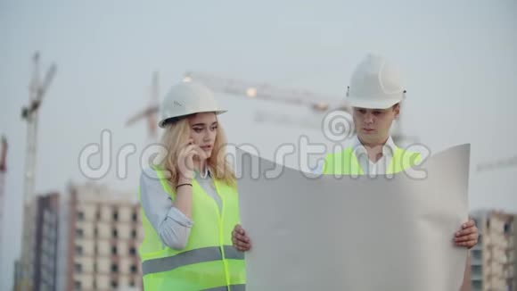 女人在打电话问建筑工人在下面的建筑物背景上的图纸上有什么视频的预览图