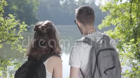 男人和年轻可爱的女孩站在森林的河岸上背包指向别处的肖像年轻人视频的预览图