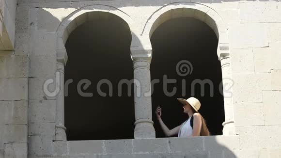 戴帽子的年轻女人自拍坐在老窗的拱门里夏日阳光明媚旅费视频的预览图