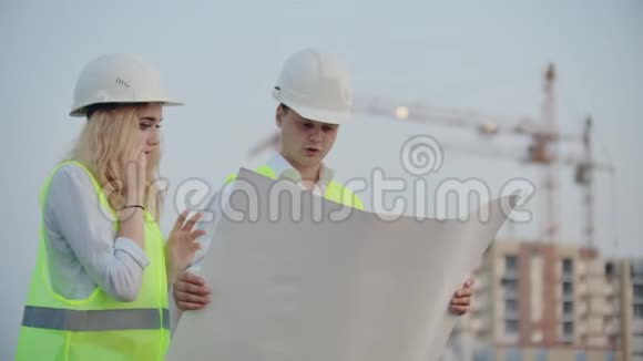 两名建筑工人在正在施工的建筑背景上画着头盔和背心一名妇女视频的预览图