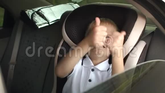 一个快乐的小男孩坐在棕色的儿童汽车座椅上竖起大拇指视频的预览图