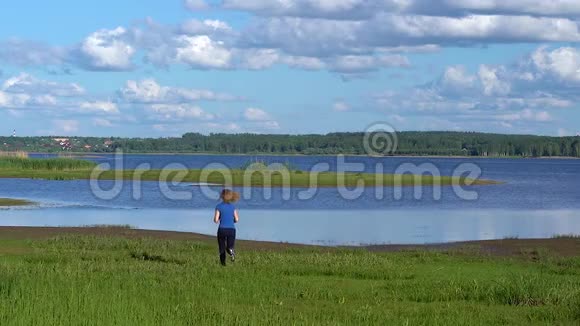 阳光明媚的一天一个穿着运动服的苗条女人跑到河边的草地上高兴地举起手来视频的预览图