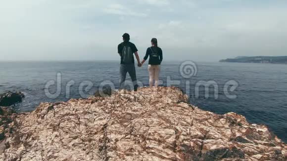 一对可爱的游客站在岩石海岸上牵手欣赏美丽的视频的预览图