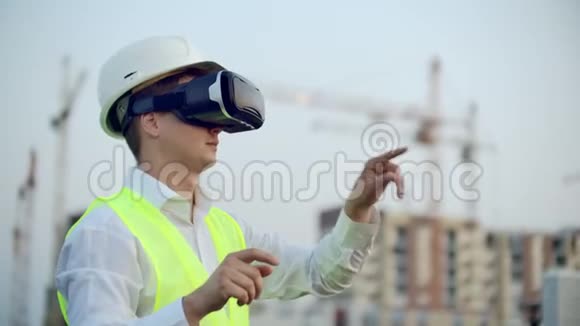 一位男性检查员用虚拟现实眼镜分析建设者工作的肖像一个戴着头盔的人和一个视频的预览图