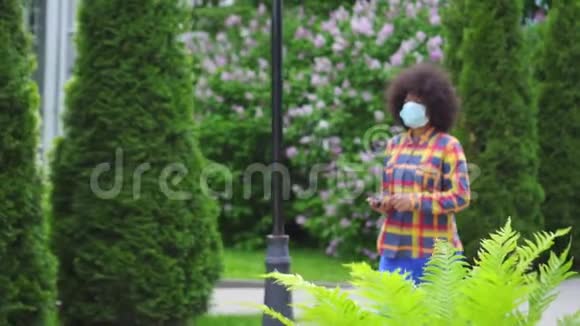 美国黑人女性留着非洲发型戴着一个带智能手机的防护口罩手里拿着慢动作视频的预览图