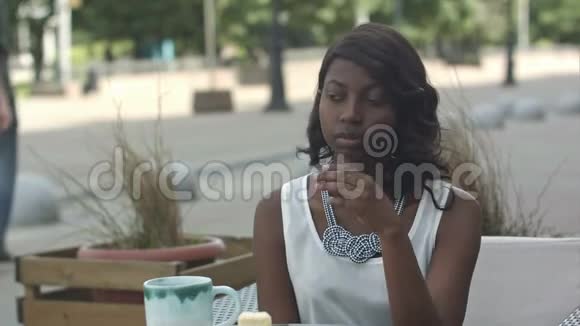 一位严肃的黑人妇女留着非洲发型穿着正式的白色上衣坐在咖啡馆等她的朋友视频的预览图