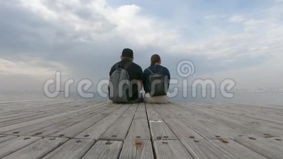 一对相爱的夫妇坐在木墩上可爱地交谈欣赏海景美丽的时光流逝视频的预览图