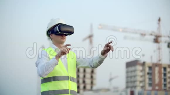 一位男性检查员用虚拟现实眼镜分析建设者工作的肖像一个戴着头盔的人和一个视频的预览图