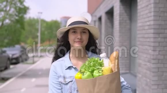 年轻漂亮的女人穿着牛仔夹克和帽子带着一个包装产品有一个好心情和微笑视频的预览图