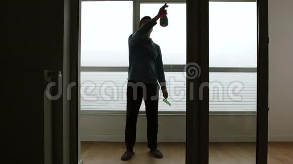 男人在大窗户上喷洒擦窗器并在白天清洗它前景视频的预览图