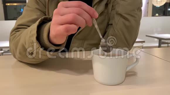 一个人在咖啡馆里用勺子搅拌咖啡中的糖在白色的杯子里餐饮理念视频的预览图