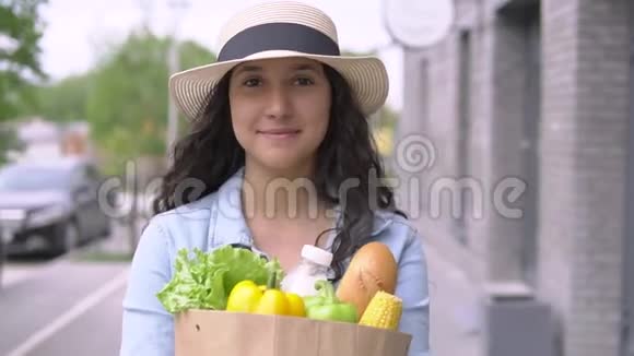 一个年轻漂亮的女人穿着牛仔夹克和帽子带着一个购物袋心情愉快微笑着关闭视频的预览图