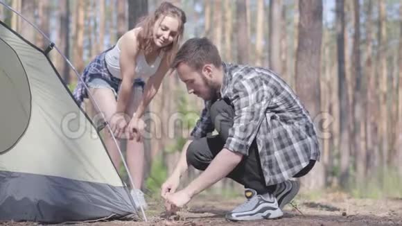 年轻人在松林里搭帐篷而他的女朋友则站在附近大自然爱好者在户外放松视频的预览图