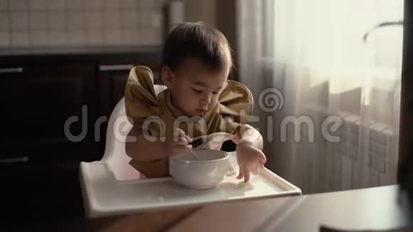 穿绿色围兜的小女孩正用手指从桌子上吃婴儿粥视频的预览图