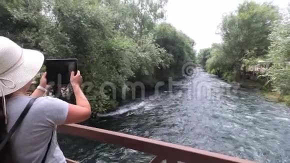 在一座横跨河流的木桥上戴着帽子的女游客头上戴着一块石碑为美丽的景色拍照视频的预览图