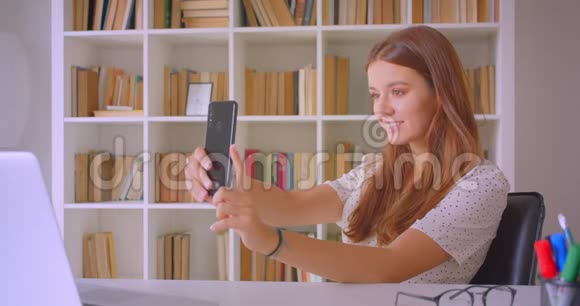 年轻的白种人女商人在手机上自拍的特写照片她开心地坐在笔记本电脑前视频的预览图