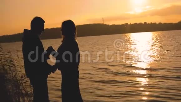 一对夫妇的剪影站在湖边夕阳下亲吻和抚摸视频的预览图