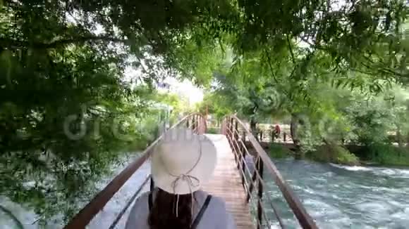 一位戴着帽子的背包的游客沿着河上的木桥慢慢地走着欣赏着美丽的景色视频的预览图