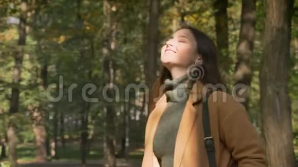 走着的白种人黑发女人微笑着脸上有阳光在公园里放松自然视频的预览图