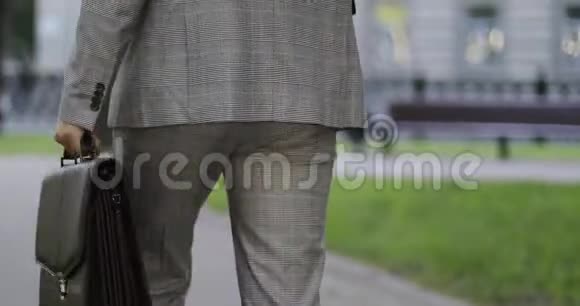 一个穿西装的商人用公文包在公园里散步的特写镜头视频的预览图
