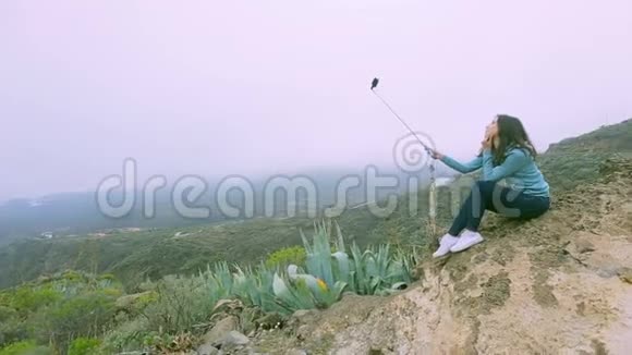 女孩用一根自拍棒在加拿大火山的绿色岩石背景上视频的预览图