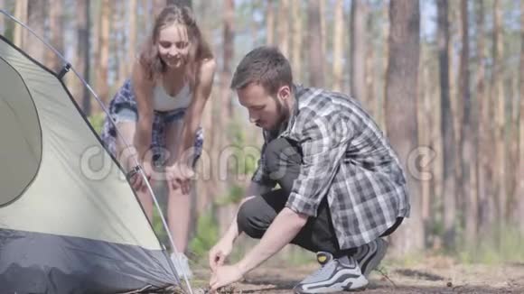 年轻人搭起帐篷而他的女朋友站在松林附近试图帮忙大自然爱好者视频的预览图