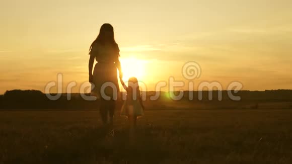 小女儿和妈妈牵着手在田野里走来走去婴儿牵着妈妈的手幸福的一家人傍晚走出家门视频的预览图