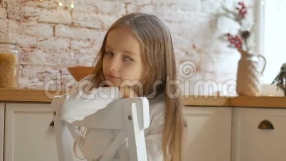 一个忧郁的小女孩蓝眼睛金发穿着白色连衣裙和毛衣坐在阁楼风格的房间里的椅子上视频的预览图