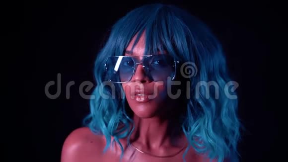 黑色墙上霓虹灯照着蓝色发型的不寻常女孩的肖像完美的化妆和假发诱惑女人视频的预览图