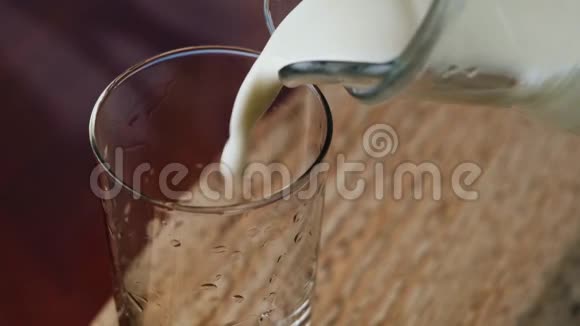 自制奶牛的牛奶从罐子里倒入玻璃杯中在木制背景上视频的预览图
