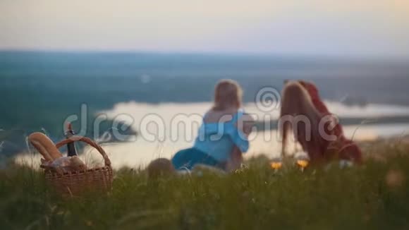 两个美丽的女人躺在田野上自拍欣赏日落时的河景视频的预览图