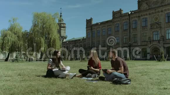 校园草坪上使用电子设备的大学朋友视频的预览图