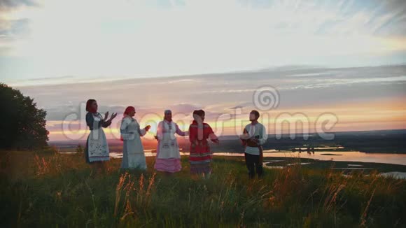 在美丽的日落背景下穿着俄罗斯传统服装的年轻人在球场上玩得很开心一个男人在玩视频的预览图