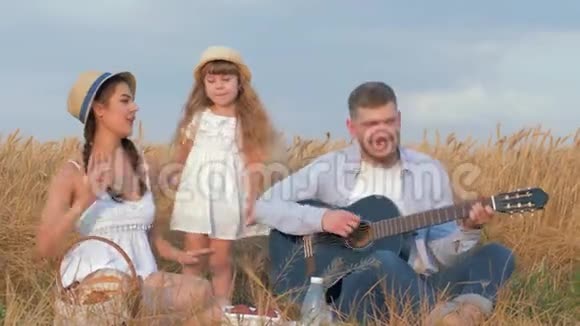 家庭田园野餐快乐的年轻夫妇可爱的小女儿演奏乐器玩得开心视频的预览图