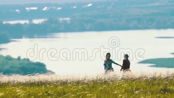 在阳光明媚的日子里两个年轻的女人在田野上拥抱湖的背景上视频的预览图